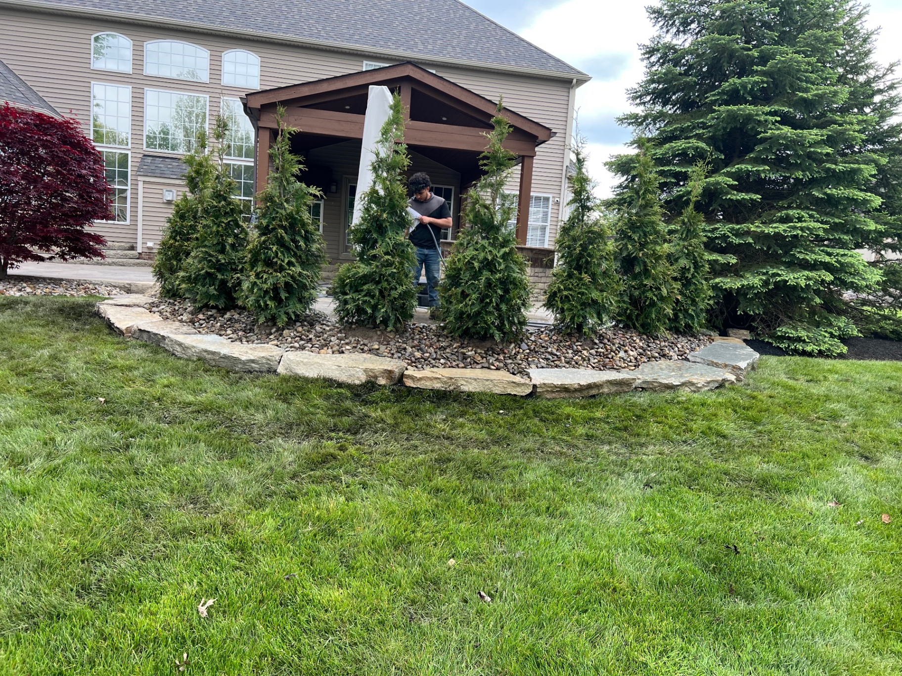 Evergreen plantings surrounded by river rock and a natural stone border beside an outdoor pavilion.