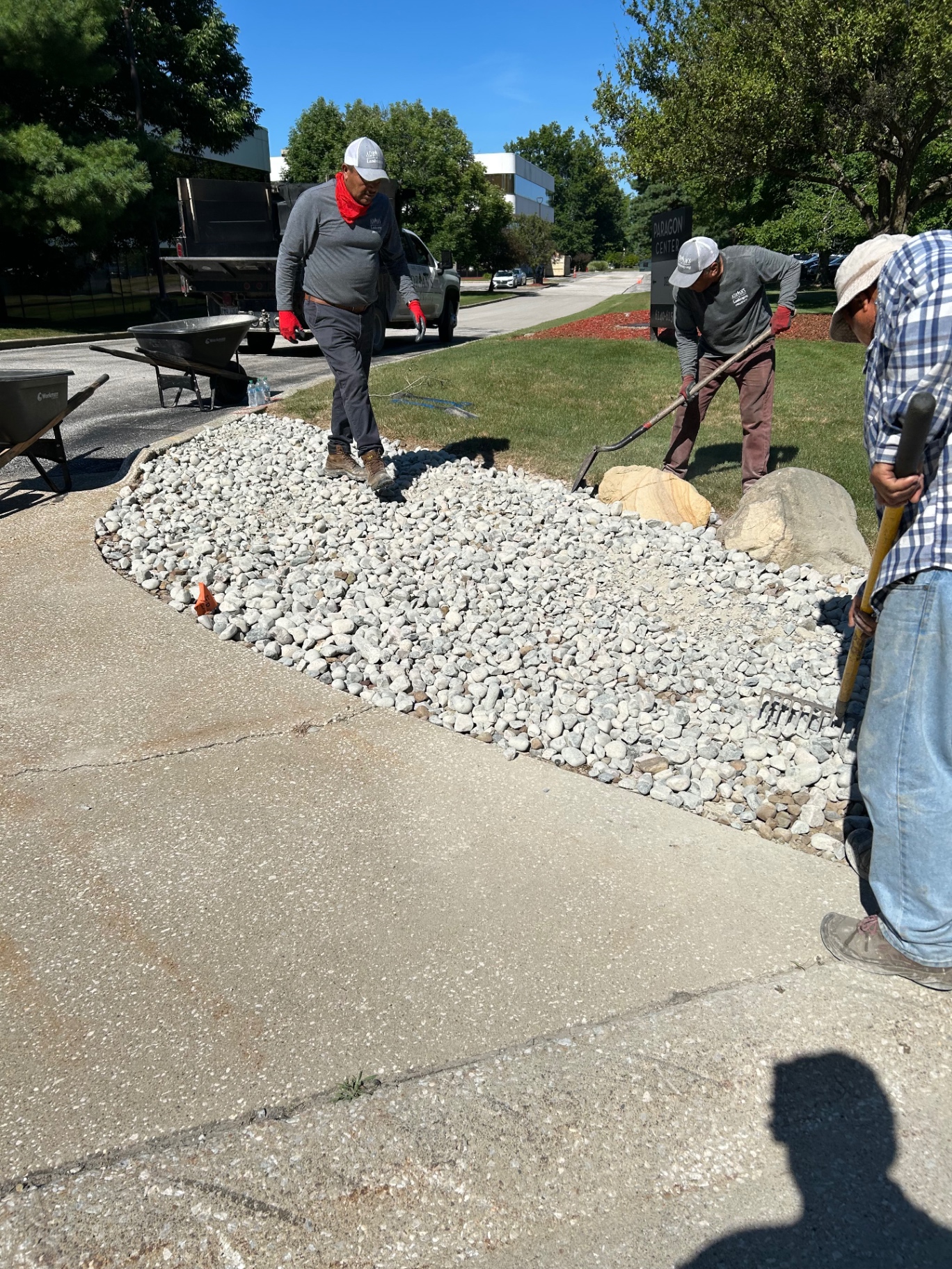 The crew spreading pale river rock around large accent boulders in a roadside landscape bed.