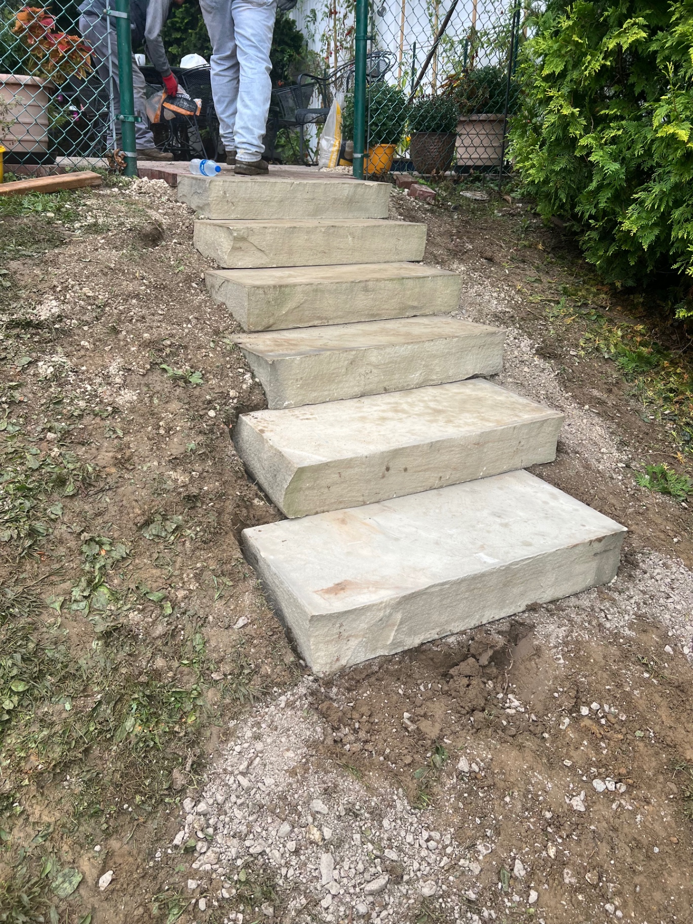 Large natural stone steps fitted into a slope leading to a garden gate, with surrounding ground still being finished.