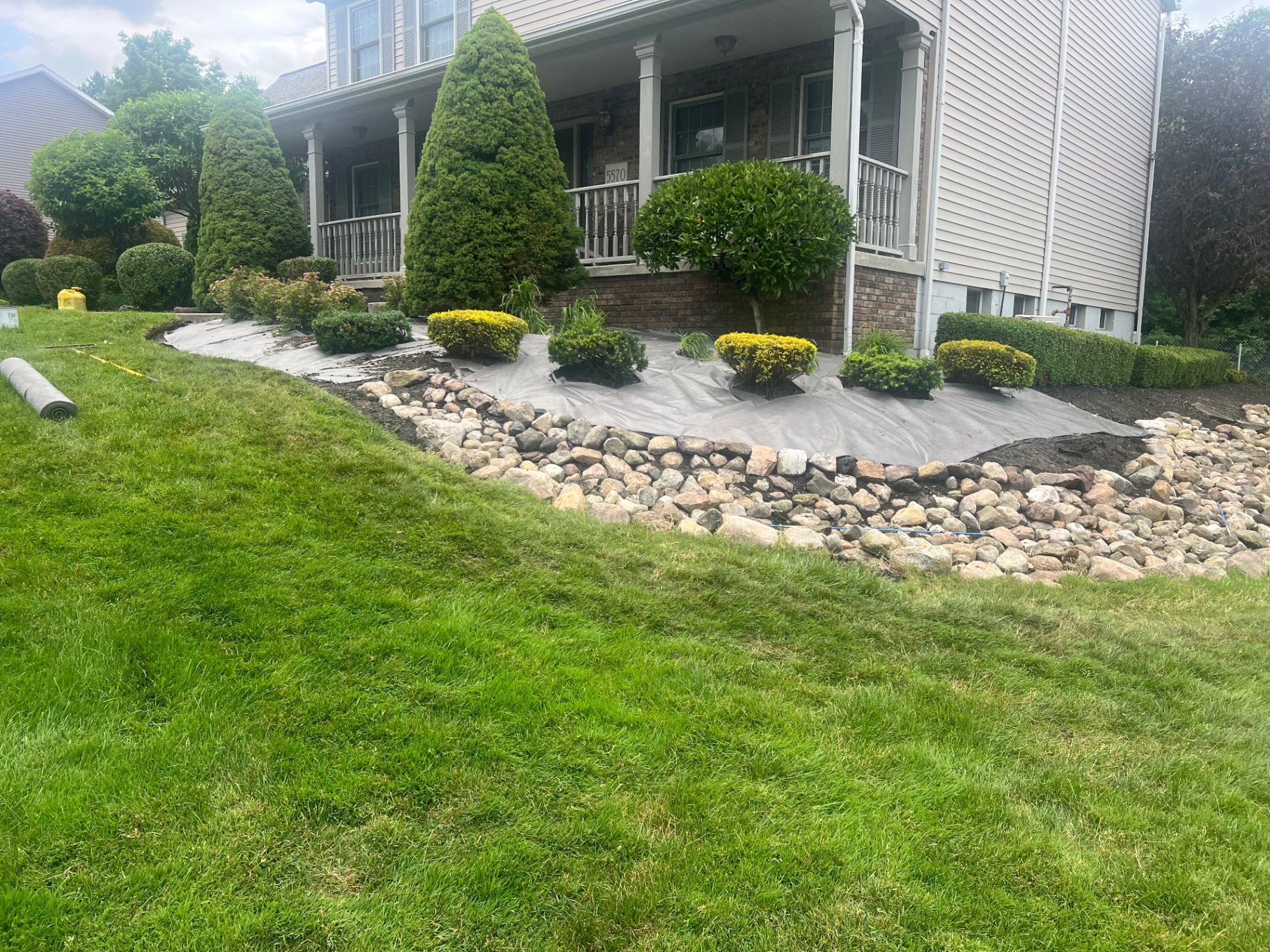Front-yard planting beds being prepared with landscape fabric and a curved river-rock border.
